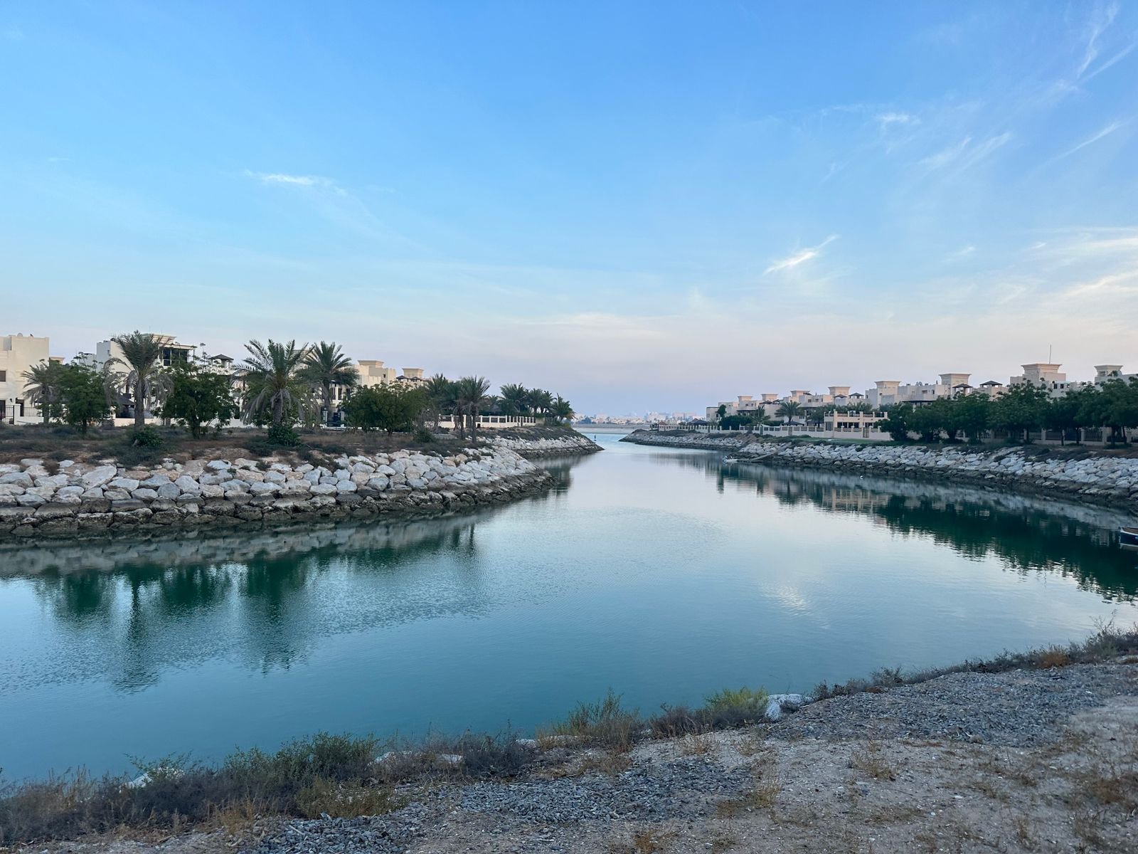 Waterway running through a low-rise residential area in Ras Al Khaimah, lined with palms under a clear sky.